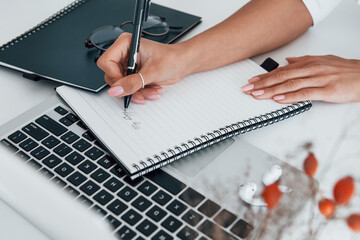 Using laptop and notepad. Young female freelancer working indoors in the office at daytime