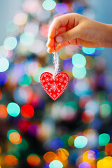 hand holding a wooden Christmas tree toy in the shape of a heart on a background of Christmas tree lights, valentine's day is coming
