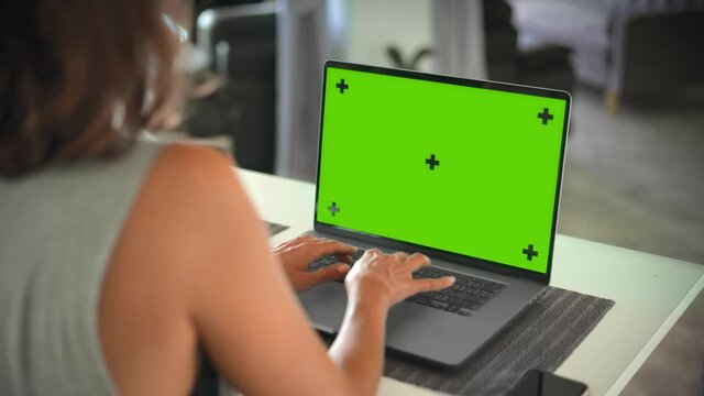 Woman typing on laptop with green screen mock up on table in bright room