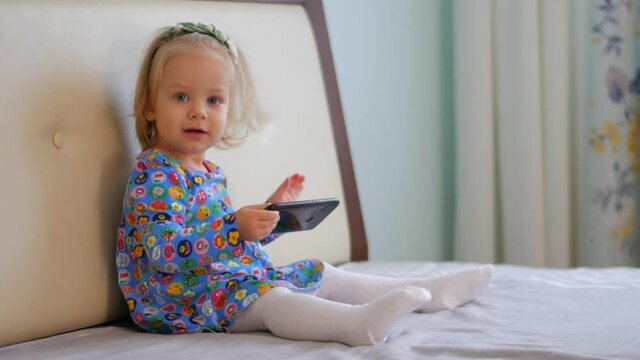 Little girl playing phone on the bed. Cute baby watching cartoons on the phone.