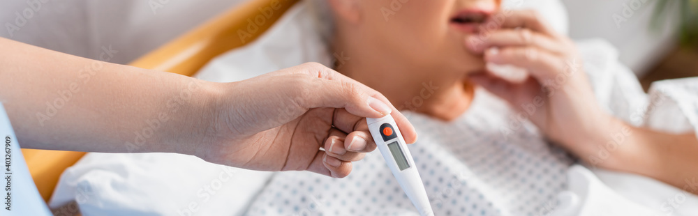 Sticker partial view of nurse holding thermometer near diseased senior woman on blurred background, banner