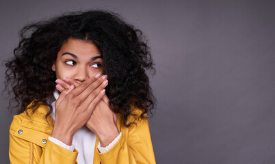 Mysterious dark-skinned young girl closes her mouth with her hands.