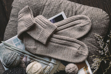 A pair of hand knitted socks with yarn balls and knitting needles. Natural colors.