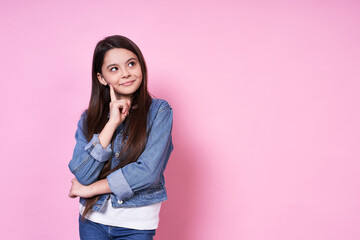 Cute emotional caucasian girl in a jeansjacket on a pink background.