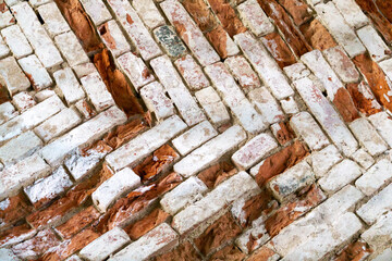 Old masonry wall of red bricks in the shape of a herringbone.