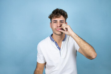 Young handsome man wearing a white t-shirt over blue background with mouth and lips shut as zip...