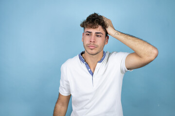 Young handsome man wearing a white t-shirt over blue background putting one hand on her head...