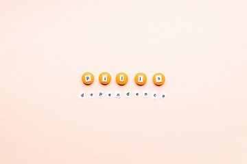 Obraz premium words pills dependence on orange pills over pink background. creative medicine and drug concept. pharmacy conceptual. above view