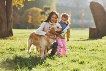 Mother with her daughter have walk with Golden Retriever dog in the park