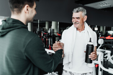 Portrait of an older man and his fitness trainer, they are shaking hands with a smile. Focus on the older man