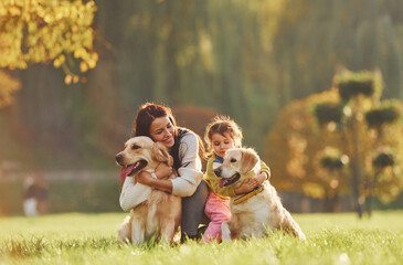 Mother with her daughter have walk with two Golden Retriever dogs in the park