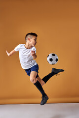 Fototapeta na wymiar soccer player boy is jumping with ball, practice and training before match, in studio