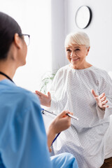 happy elderly woman smiling and gesturing while talking to nurse on blurred foreground