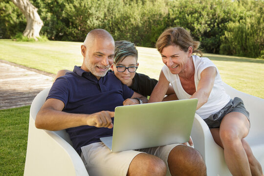Padre , madre e figlio si divertono a guardare qualcosa di interessante nel computer portatile seduti in relax nel giardino di casa