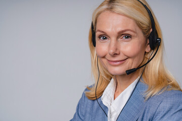 Aged beautiful call center worker in formal attire with headphones isolated over grey background - Powered by Adobe