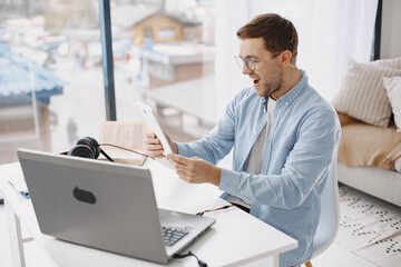 Man sitting in living room at home. Guy enjoying studying using laptop and headset. Man use a tablet.