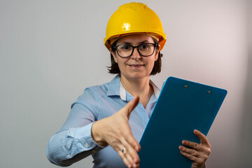 Portrait of friendly pretty female engineer wearing a safety yellow helmet standing, 