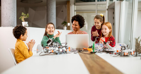 Happy kids with their African American female science teacher with laptop programming electric toys and robots at robotics classroom