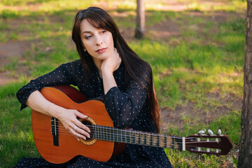 A woman is sitting in the park on the grass with an acoustic guitar. Girl musician