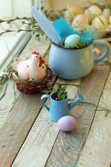 Easter composition of feathers, a cup with eggs, hay and decorations on a wooden surface against the background of a window, the concept of congratulations, postcard