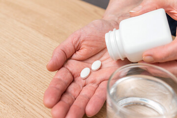 White pills of painkiller or antibiotic for treatment on senior woman hand palm, glass with water, medicines and vitamin supplements concept,close-up view