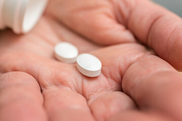 White pills of painkiller or antibiotic for treatment on senior woman hand palm, medicines and vitamin supplements concept, close-up view