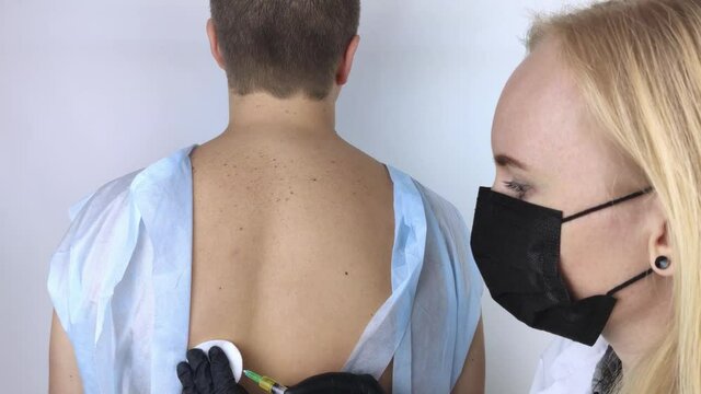 The infectious disease doctor makes a medical vaccination to the patient in the scapula. Immunization against tetanus, influenza, diphtheria, tick-borne encephalitis and hepatitis B