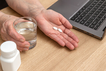 White pills of painkiller or antibiotic for treatment on senior woman hand palm, glass with water,...