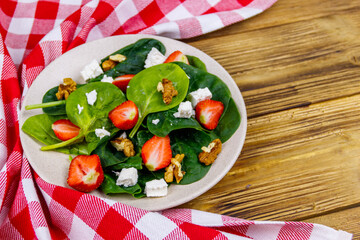 Fresh healthy salad with strawberry, spinach, walnuts and feta cheese on wooden table