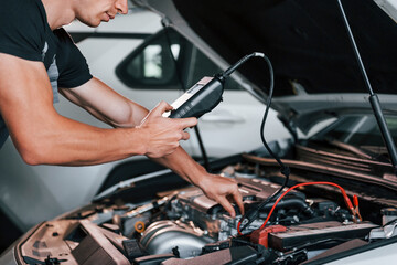 Fototapeta na wymiar Tests car's electronics. Adult man in grey colored uniform works in the automobile salon