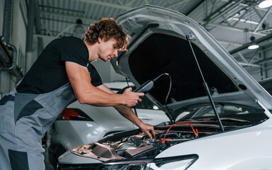 Fototapeta na wymiar Tests car's electronics. Adult man in grey colored uniform works in the automobile salon