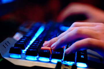 Close-up on human hands on a neon lit keyboard. Multifunction keyboard with set of red button. WASD keys are used in many video games. 