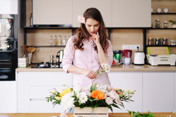 Florist at work: pretty young brunette woman making fashion modern composition of different flowers at home