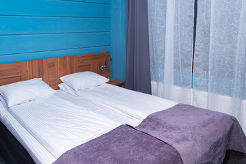 The double bed is made with linen sheets. The interior of the bedroom. Double bed in the hotel room. White bed linen and lilac blankets on the bed.
