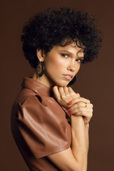  Vertical photo of a curly-haired female model in a studio in brown tones