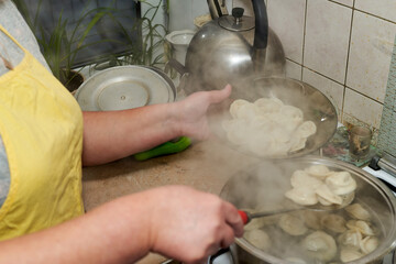 A woman takes out cooked dumplings from a pan into a transparent plate - 403282944