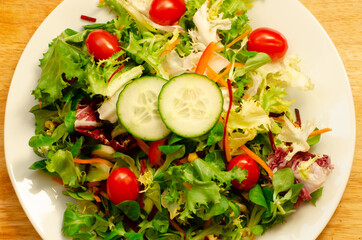 White plate with fresh leafy salad, tomato and cucumber
