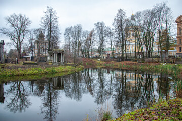 Fototapeta na wymiar An autumn view on the Monastery Island with churches at the back and an old cemetery reflecting in the pond, Saint Petersburg, Russia