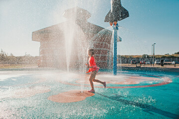 Cute adorable Caucasian funny girl playing on splash pad playground on summer day. Happy child...