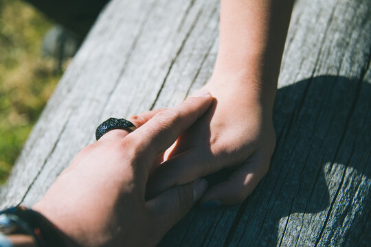 Young couple's hands on a dry tree trunk, the man wears different rings.