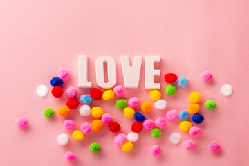 Bright creative card for Valentine's Day. The inscription Love in multi-colored pom-poms on a pink background. Valentines day creative concept