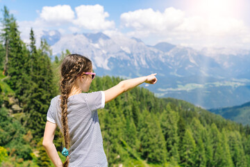 Girl hiking on beautiful summer day in alps mountains Austria, resting on rock and admire amazing view to mountain peaks. Active family vacation leisure with kids. Outdoor fun and healthy activity