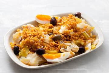 cod fish with sweet potato, boiled egg, olives and corn bread on white dish