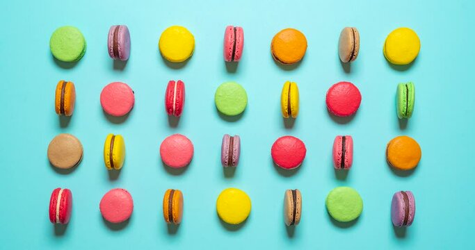 Macarons moving stop motion. Top view with multi-colored macarons. Flat lay with macarons of various colors flipping on the side. Delicious homemade macarons isolated on a blue background.