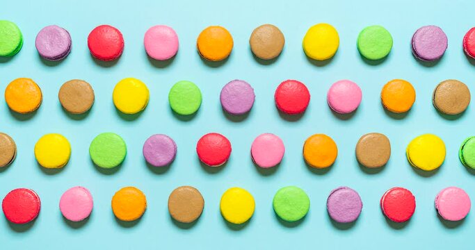 Macarons in a row stop motion. Multi-colored macaroons top view. Macarons of various colors on a blue background moving from left to right, stop motion video. 
