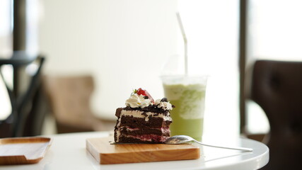Chocolate cake sliced on wood plate with cold green tea milk in plastic cup in coffee shop.