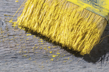 A paintbrush dipped in yellow paint lies on a gray board. Colored in 2021 color trends Ultimate Gray and Illuminating.