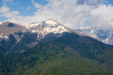 Snow-capped mountains and green forest. The Caucasus mountain range. Spring bright sunny day in the mountains. Colorful landscape in spring.The concept of ecotourism, travel, winter outdoor activities