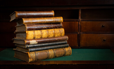 Vintage books stack on old wooden surface in warm directional light. Selective focus.