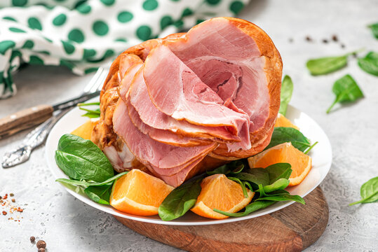 Sliced ham in a plate close-up. Baked pork ham with oranges and spinach on a gray concrete background.
